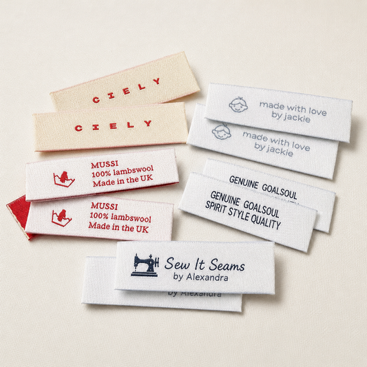Selection of personalised woven clothing labels with custom business names and logos on a cream background