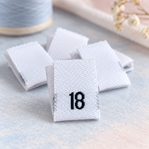White women’s woven size 18 clothing labels on a soft blue and blush background