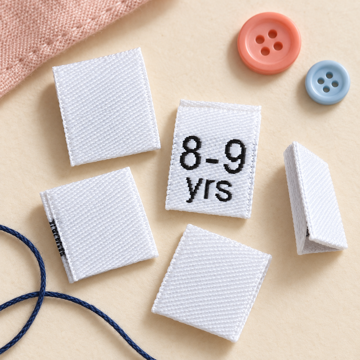 White 8–9 years kids’ woven clothing size label displayed with sewing thread and buttons