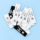Pile of black and white personalised woven labels with sewing-themed branding on a light blue background