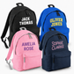 Four personalised children’s backpacks in black, royal blue, pink and navy, each printed with a name in a different font and colour.