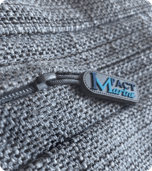 Custom silicone zipper pull branded Mact Marine attached to a grey textured bag