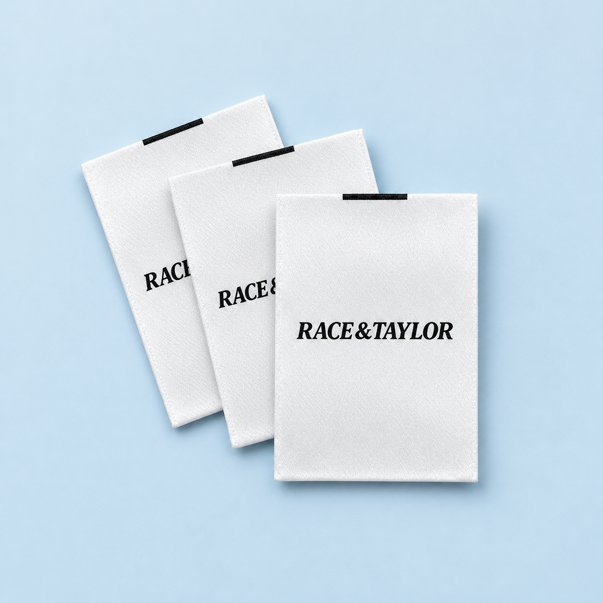 White custom printed satin clothing labels with black branding on a pale blue background