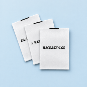 White custom printed satin clothing labels with black branding on a pale blue background