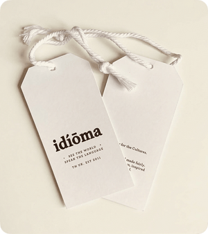 Two custom printed white silk swing tags with white cord on a cream background