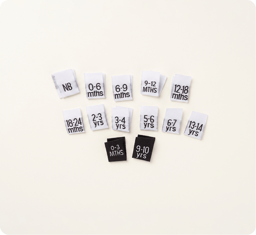 Assorted black and white kids’ woven clothing size labels from newborn to 13–14 years on a cream background