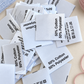 Pile of white printed satin care labels with clothing composition, washing instructions and laundry symbols