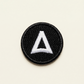 Round black embroidered fabric badge with a white logo
