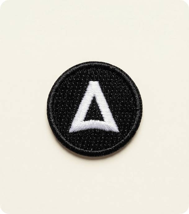 Round black embroidered fabric badge with a white logo