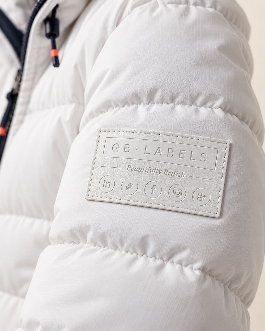 White custom leather GB Labels patch sewn onto the sleeve of a snow-white padded parka jacket